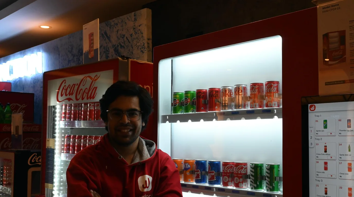 Worker restocking fresh-food jars into a refrigerated vending machine at dawn