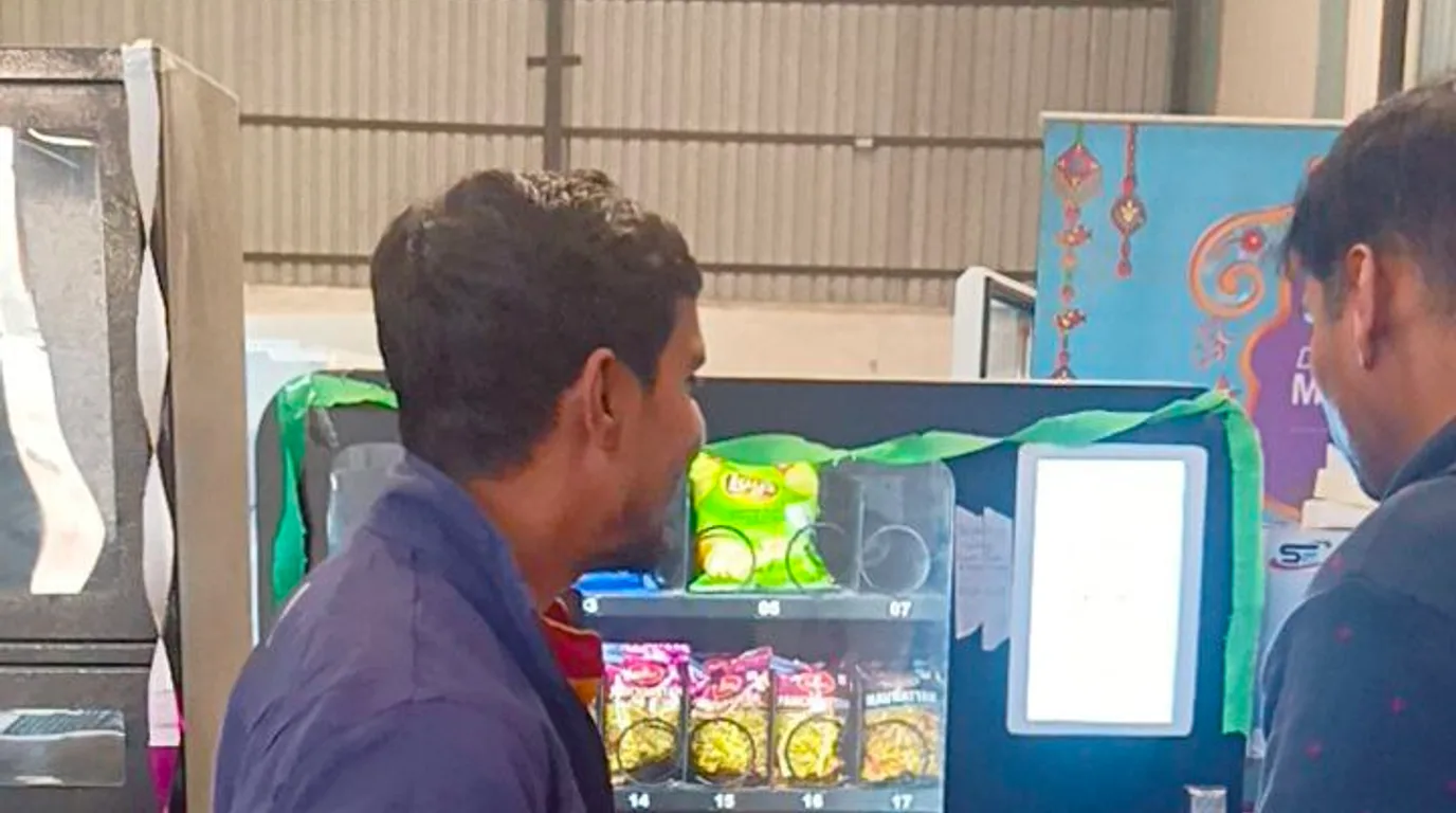 Hands counting rupee notes beside a model vending machine and a calculator