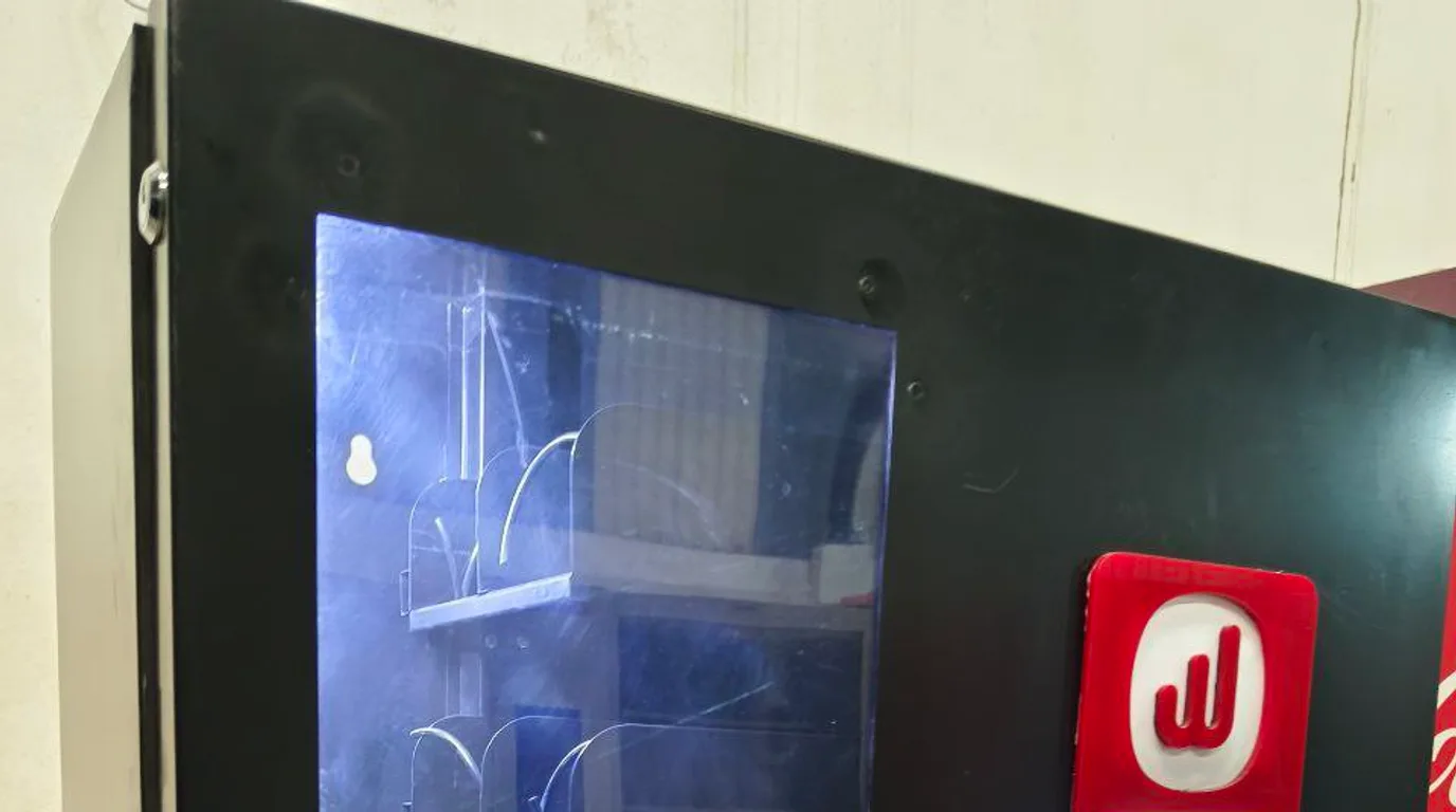 Technician securing a modern vending machine to a wall with an anti-tip bracket