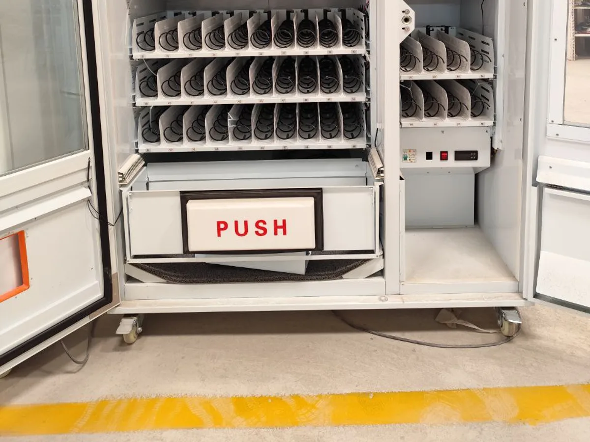 Buyer and technician inspecting the open interior and coil motors of a vending machine.
