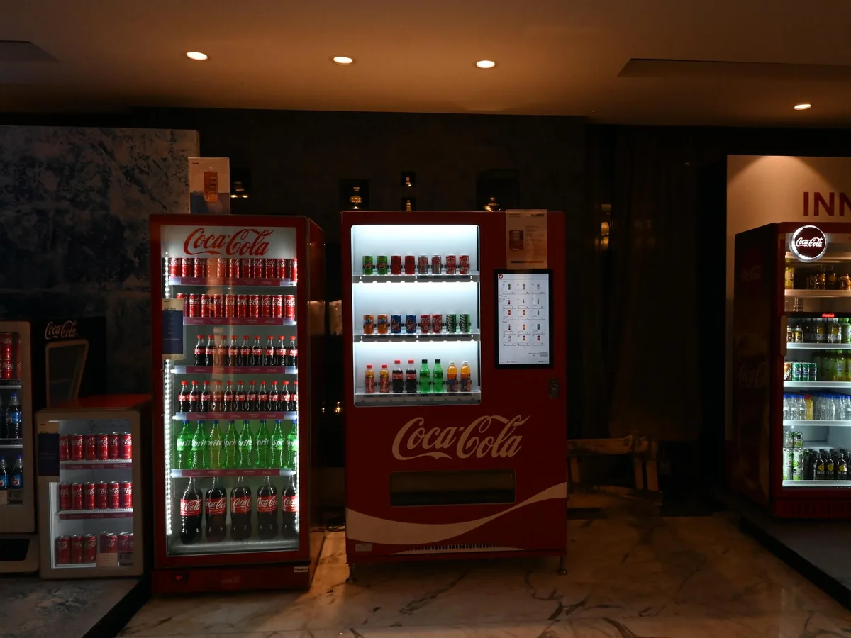 Operator adjusting drink prices at the coin door of a cold-drink vending machine.