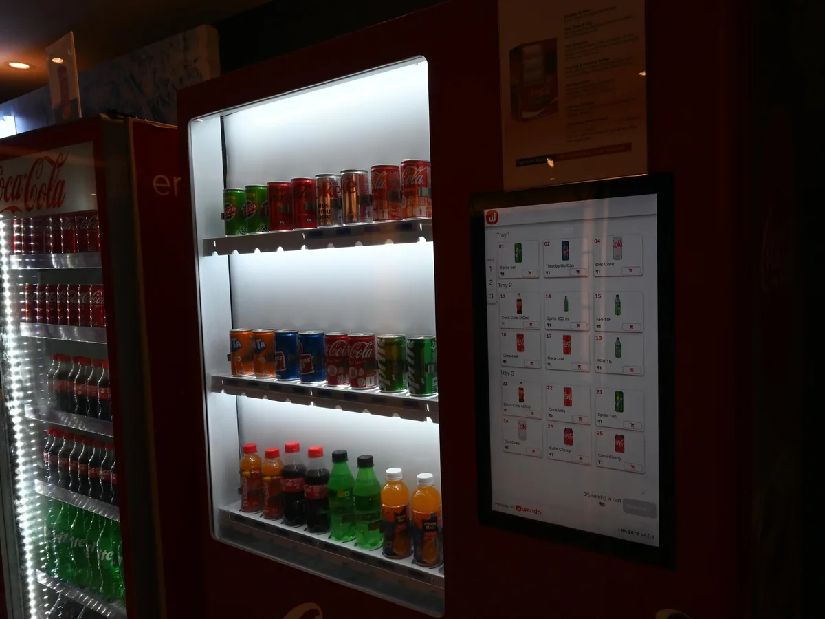 Operator cleaning an infrared sold-out sensor inside a vending machine tray with a swab.