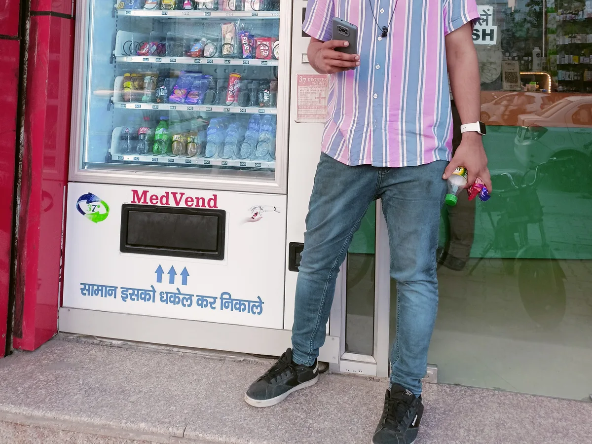 Operator restocking a vending machine while checking an inventory app on a phone