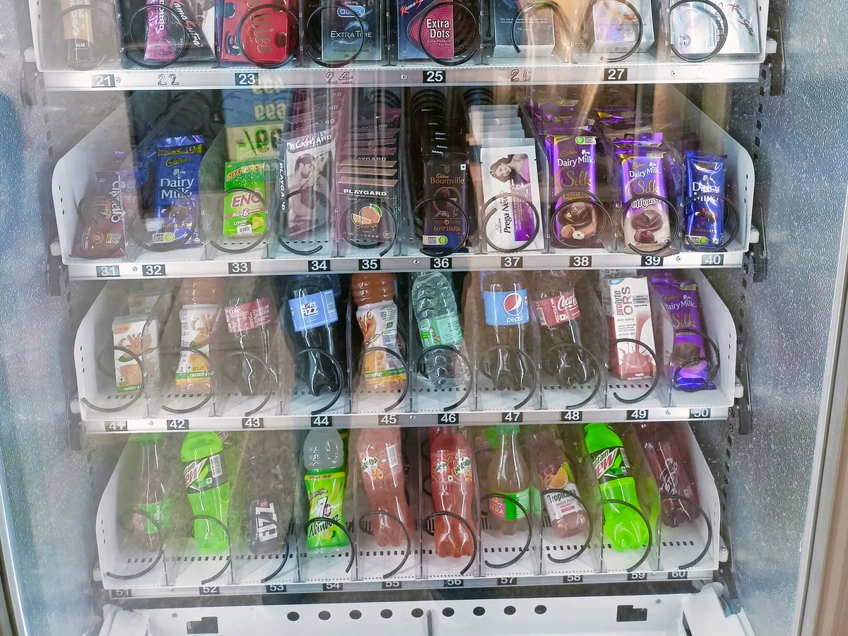 Customer collecting a snack from a vending machine in a busy campus
